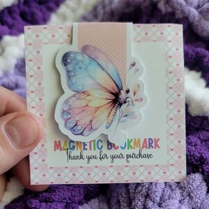 Colorful butterfly magnetic bookmark with pastel wings on a pink polka dot background.