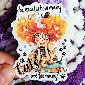 A whimsical redhead surrounded by many playful cats, with the text "So, exactly how many cats are too many?"