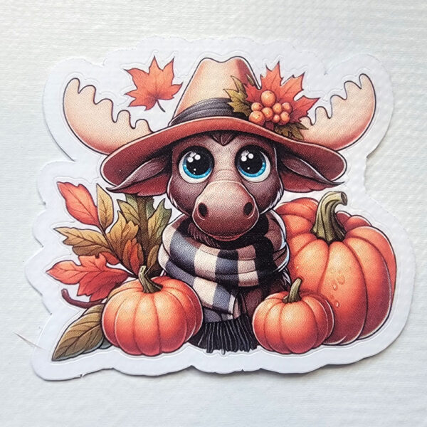 Vinyl sticker of a cute moose wearing a hat and scarf, surrounded by pumpkins and autumn leaves.