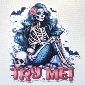 Sticker of a skeleton mermaid with long wavy hair, a floral headpiece, and "Try Me!" text, surrounded by seashells and skulls.